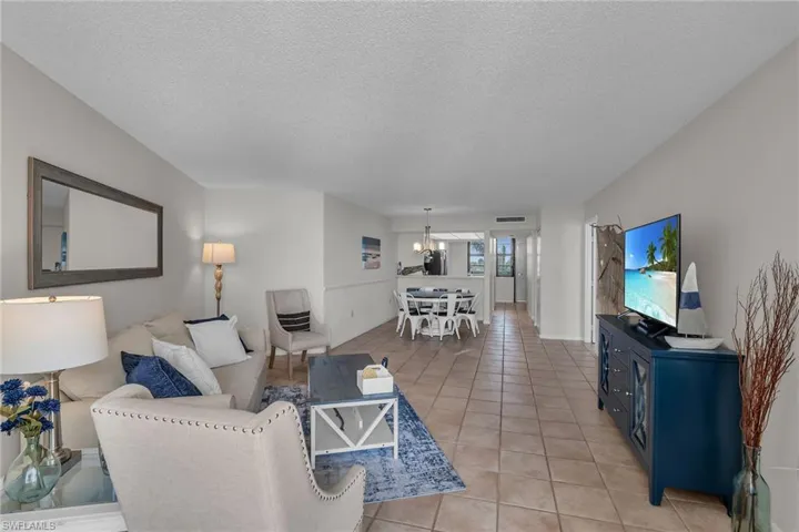 Living area with a textured ceiling, an inviting chandelier, light tile patterned floors, and visible vents
