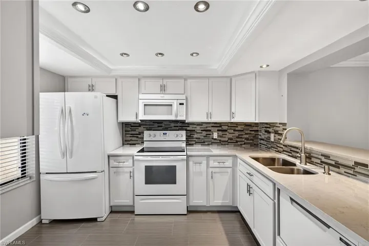 Kitchen featuring white appliances, light stone counters, crown molding, white cabinetry, and tasteful backsplash