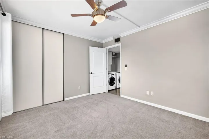 Unfurnished bedroom with crown molding, carpet, a ceiling fan, washer and dryer, and a closet