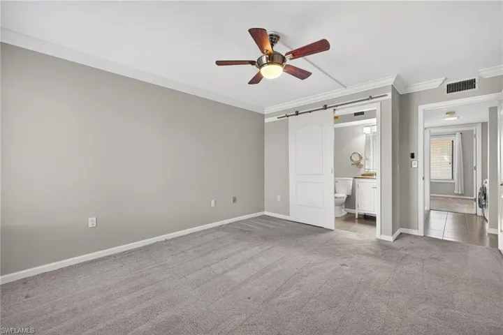 Unfurnished bedroom featuring a barn door, crown molding, carpet floors, a ceiling fan, and ensuite bath