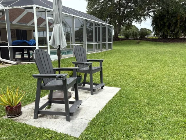 View of green lawn with an outdoor pool, a patio, and glass enclosure