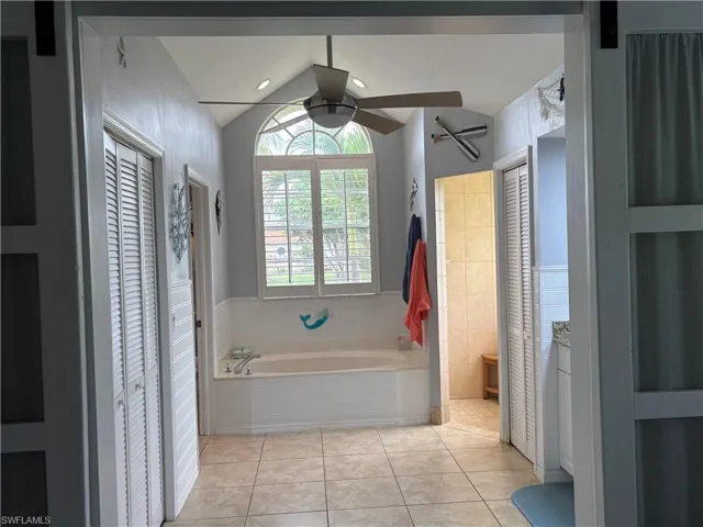 Bathroom featuring a closet, a tub, ceiling fan, lofted ceiling, and