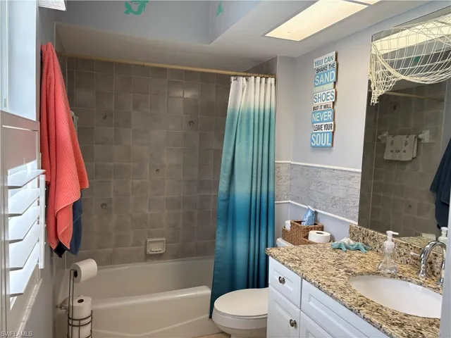 Bathroom with vanity, tile walls, toilet, shower / tub combo with curtain, and a wainscoted wall