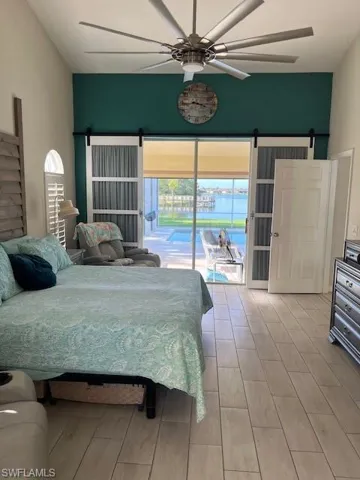 Bedroom featuring a barn door, access to outside, a ceiling fan, and wood finish floors