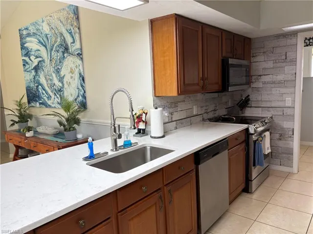 Kitchen with stainless steel appliances, a sink, light tile patterned flooring, and light countertops