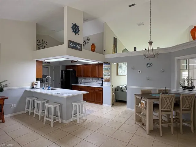Kitchen with freestanding refrigerator, high vaulted ceiling, a sink, a peninsula, and light tile patterned floors