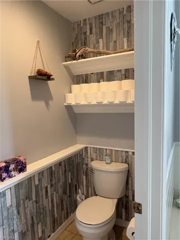 Bathroom with a wainscoted wall, toilet, tile patterned floors, and wooden walls