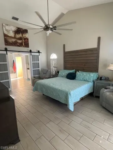 Bedroom with a barn door, high vaulted ceiling, wood tiled floors, and ceiling fan
