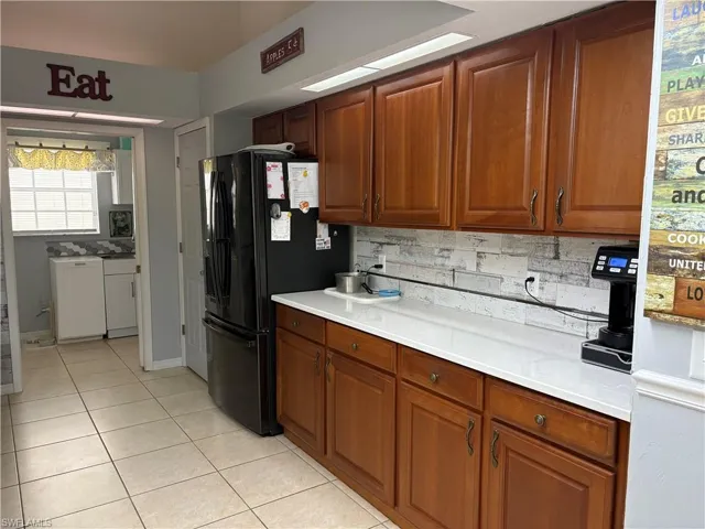 Kitchen with light tile patterned flooring, black refrigerator with ice dispenser, light countertops, tasteful backsplash, and brown cabinetry