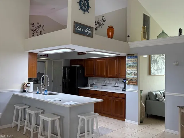 Kitchen featuring high vaulted ceiling, black fridge with ice dispenser, a sink, light countertops, and a peninsula