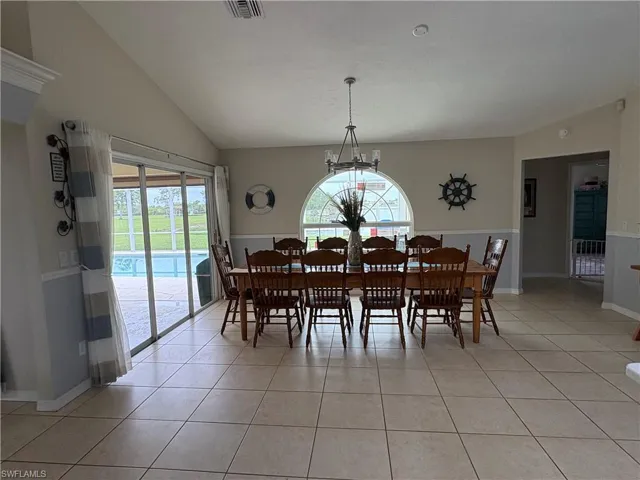 Dining space featuring plenty of natural light, light tile patterned floors, lofted ceiling, a chandelier, and baseboards