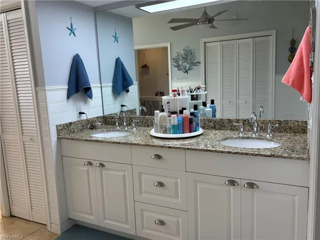 master featuring dual sinks bathroom featuring a closet, double vanity, ceiling fan, tile patterned floors, and wainscoting