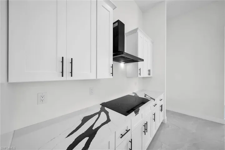 Kitchen with white cabinets, light stone counters, black electric stovetop, and wall chimney range hood