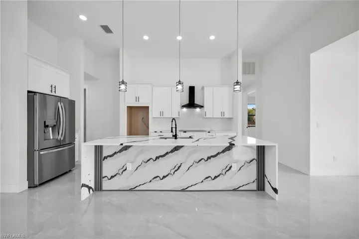 Kitchen with white cabinets, hanging light fixtures, stainless steel fridge, and wall chimney range hood