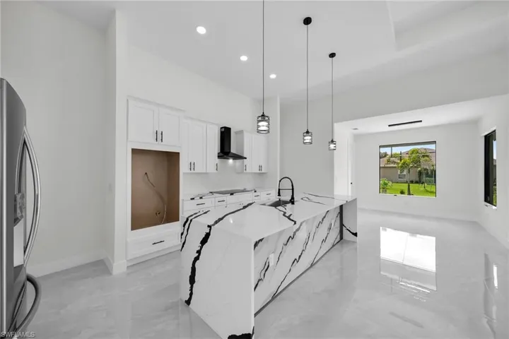 Kitchen featuring light stone counters, white cabinets, pendant lighting, stainless steel refrigerator with ice dispenser, and wall chimney range hood