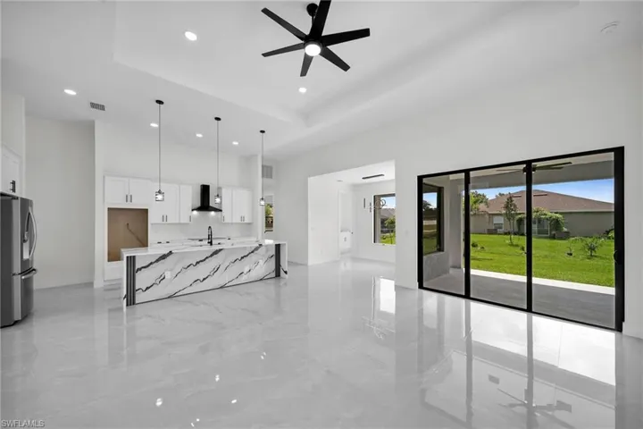 Kitchen featuring light stone counters, white cabinets, wall chimney exhaust hood, decorative light fixtures, and stainless steel fridge with ice dispenser