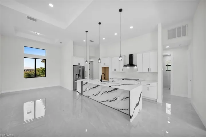 Kitchen featuring white cabinetry, wall chimney exhaust hood, stainless steel refrigerator with ice dispenser, sink, and a spacious island