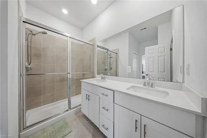 Full bathroom featuring double vanity, a shower stall, and light tile patterned floors
