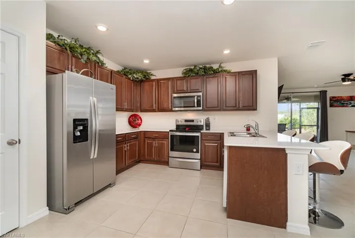 Kitchen featuring sink, light tile patterned floors, appliances with stainless steel finishes, a kitchen bar, and kitchen peninsula