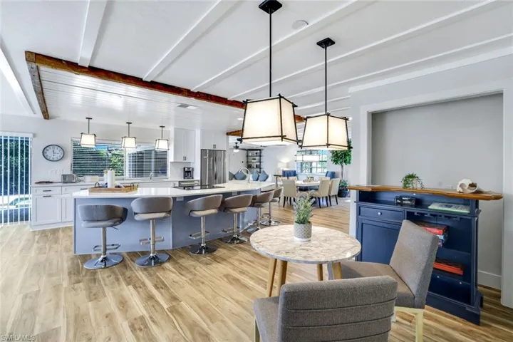 Kitchen featuring a breakfast bar area, pendant lighting, light wood-type flooring, white cabinets, and beamed ceiling