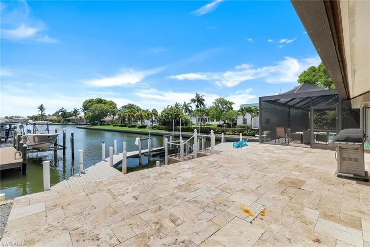 Dock with glass enclosure, a sunroom, a water view, boat lift, and a patio area