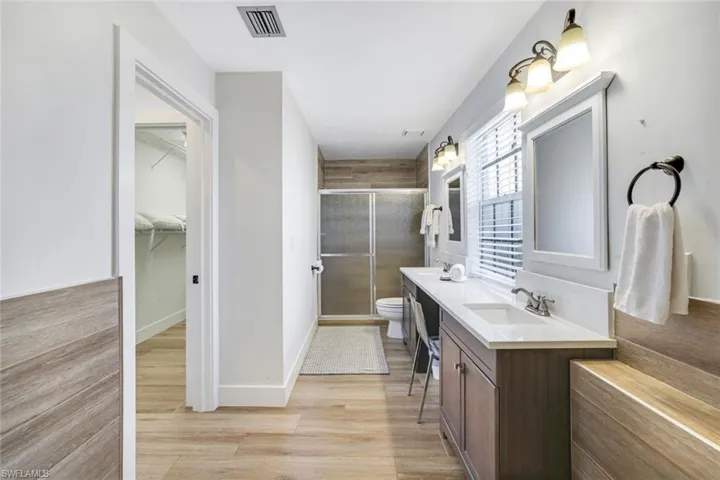 Full bath featuring double vanity, a shower stall, light wood-style flooring, and a spacious closet
