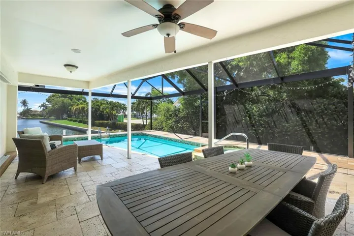 Outdoor pool featuring a patio area, glass enclosure, a sunroom, outdoor dining space, and a water view