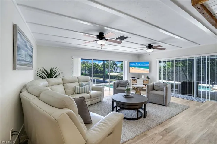 Living area with a ceiling fan, light wood-type flooring, and beam ceiling