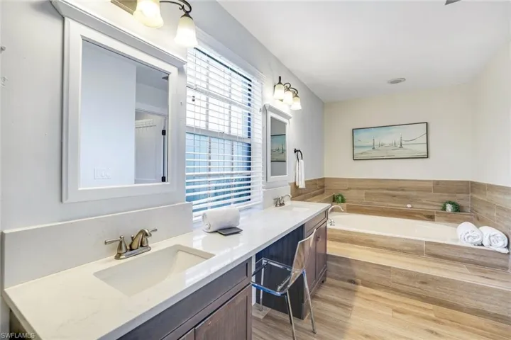 Bathroom with double vanity, a bath, and light wood-type flooring