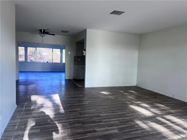 Empty room featuring ceiling fan, visible vents, dark wood finished floors, and baseboards