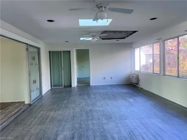 Empty room featuring a skylight, a ceiling fan, baseboards, a wall mounted air conditioner, and dark wood finished floors