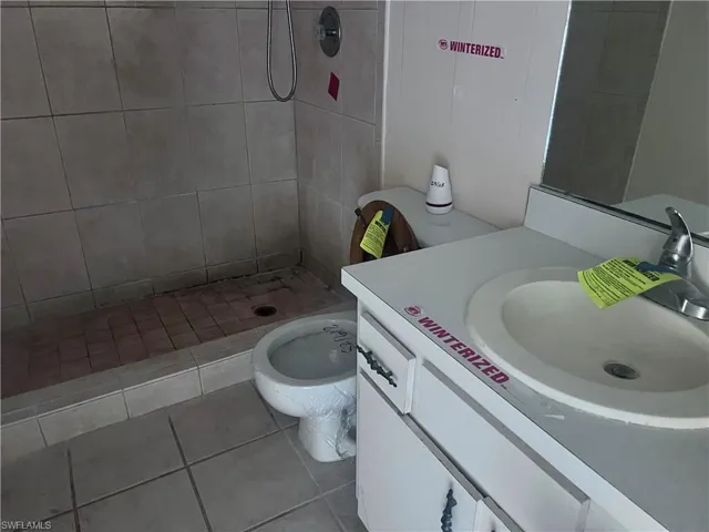 Bathroom with toilet, tile patterned flooring, a tile shower, and vanity