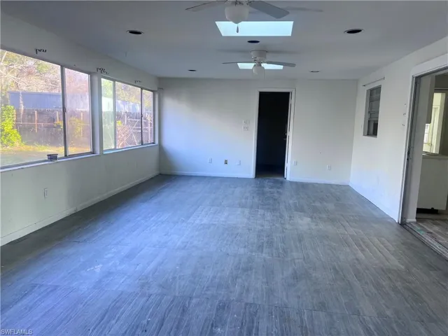 Empty room featuring a skylight, a ceiling fan, baseboards, and dark wood-type flooring