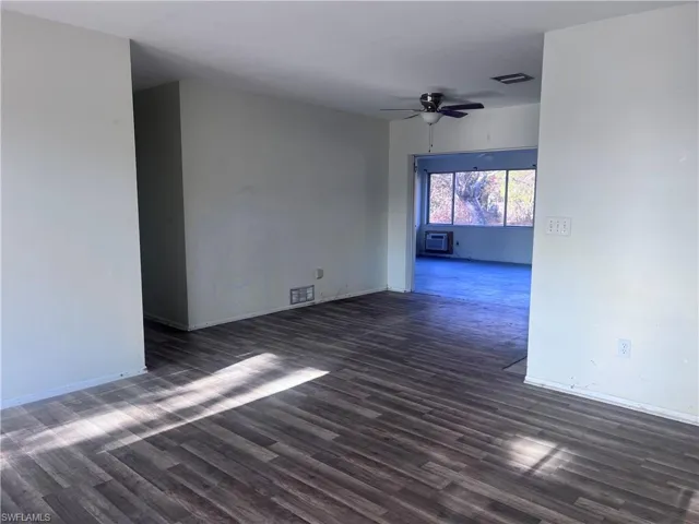 Empty room featuring dark wood-style floors, ceiling fan, visible vents, and an AC wall unit