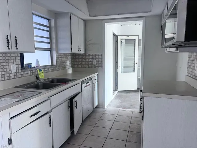Kitchen with a sink, white cabinets, light countertops, stainless steel dishwasher, and tasteful backsplash