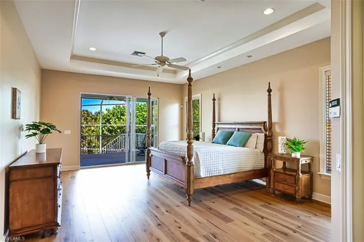 Bedroom with a tray ceiling, access to outside, light wood-type flooring, recessed lighting, and a ceiling fan