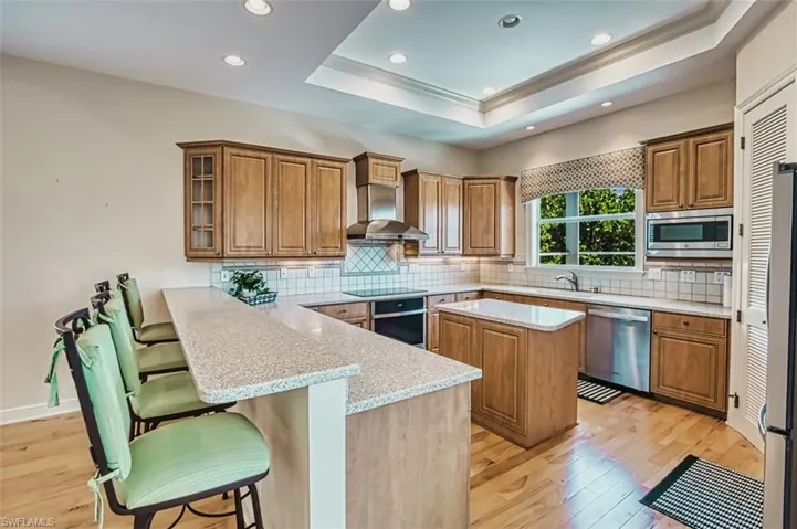 Kitchen with a peninsula, light wood-style floors, brown cabinetry, a breakfast bar area, and light stone countertops