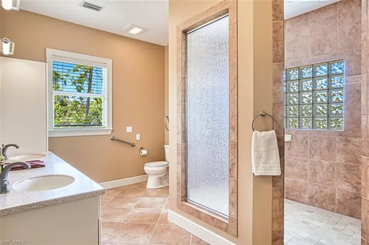 Bathroom featuring tiled shower, double vanity, and tile patterned flooring