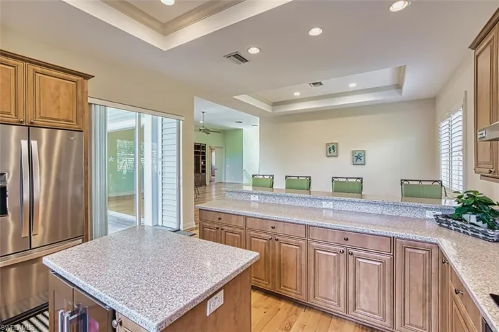 Kitchen with a raised ceiling, stainless steel fridge, light wood-style floors, recessed lighting, and a peninsula