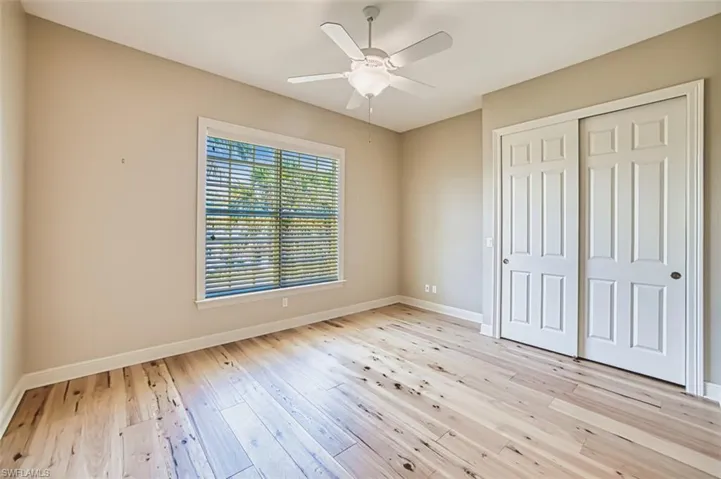 Unfurnished bedroom featuring light wood finished floors, a closet, connected bathroom, and a ceiling fan