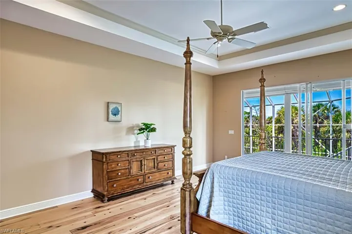 Bedroom featuring light wood finished floors, a raised ceiling, access to exterior, and a ceiling fan