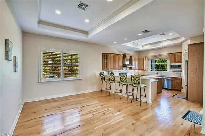 Kitchen with a tray ceiling, brown cabinetry, a breakfast bar area, a peninsula, and light wood-style flooring