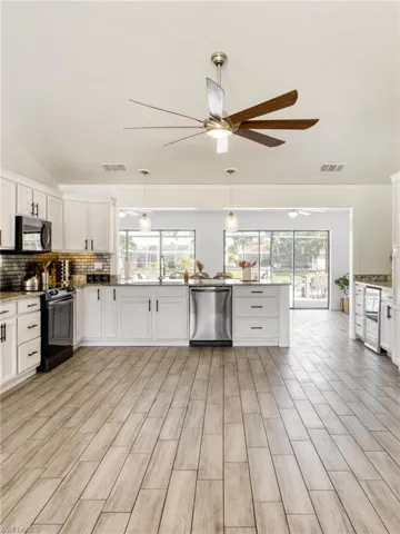 Kitchen featuring white cabinetry, black appliances, decorative backsplash, plenty of natural light, and vaulted ceiling