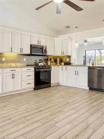 Kitchen featuring lofted ceiling, decorative light fixtures, stainless steel appliances, white cabinets, and tasteful backsplash