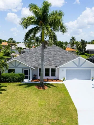 Ranch-style home with stucco siding, roof with shingles, concrete driveway, and a front yard