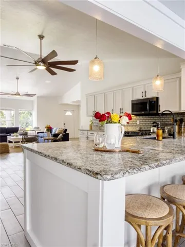 Kitchen featuring vaulted ceiling, light stone countertops, and pendant lighting