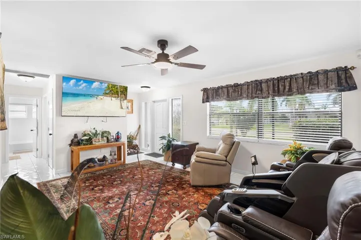 Ceiling fan with integrated lighting, wall-mounted television, tiled flooring, front entry door with glass insert, and a large window with blinds