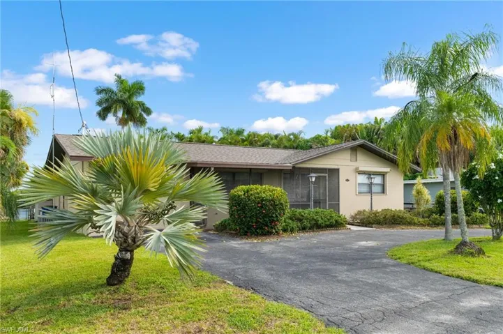 Single-story residence featuring a screened porch, mature palm trees, established landscaping, and a paved driveway