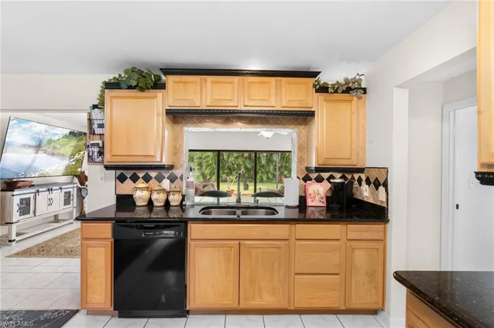 Kitchen featuring wood cabinetry, black countertops, a tile backsplash, and a double basin sink
