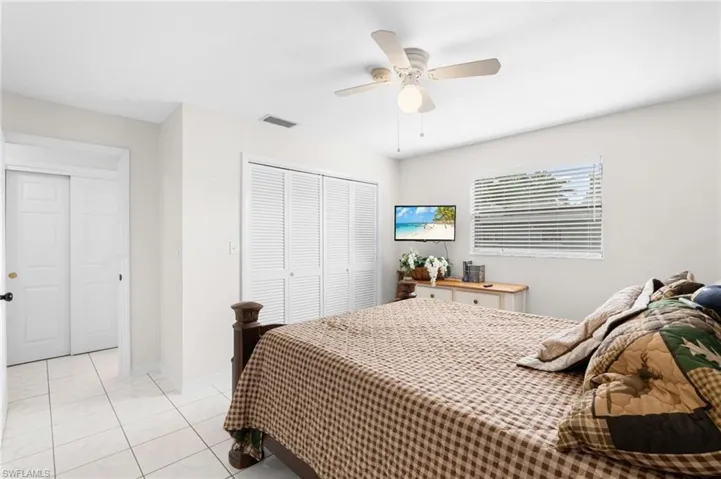 White tile flooring, louvered bi-fold closet doors, ceiling fan with integrated lighting, window with horizontal blinds, wall-mounted television